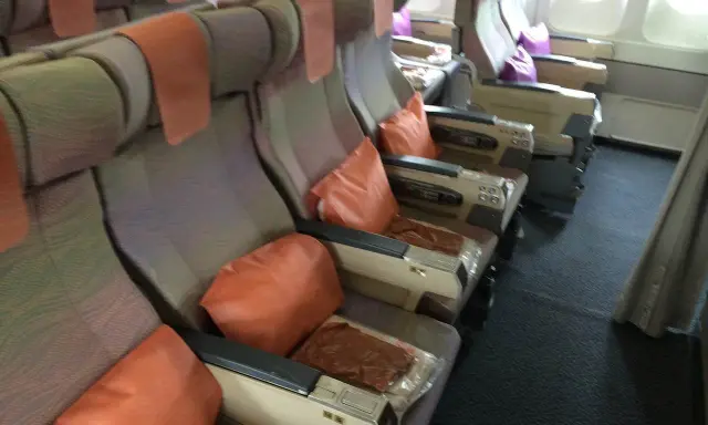Fotele w samolocie linii lotniczych Emirates, z pomarańczowymi poduszkami i zagłówkami, gotowe na podróż.