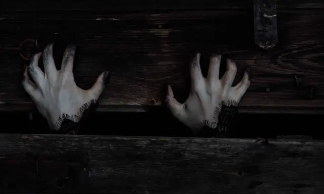 Mains pâles aux doigts noircis sortant d'une caisse en bois sombre, évoquant une musique qui fait peur au piano.