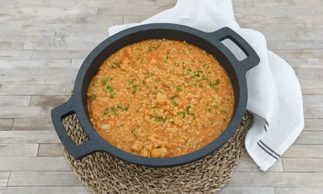 Arroz cremoso con gambones, adornado con cebollino fresco, servido en una paellera sobre una mesa de madera.