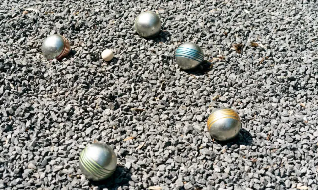 Boules de pétanque argentées, certaines rayées de couleurs vives, reposent sur un lit de gravier gris. Le jeu de pétanque est prêt à commencer.