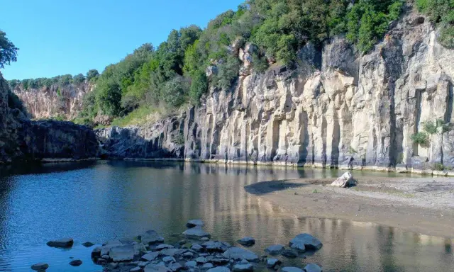 Un'oasi naturale nella Tuscia: un fiume serpeggia tra imponenti pareti rocciose ricoperte di vegetazione, creando uno scenario suggestivo.
