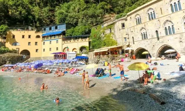 Ein idyllischer **Geheimtipp Italien Strand** mit bunten Sonnenschirmen, sonnenbadenden Menschen und kristallklarem Wasser vor malerischer Kulisse.