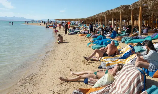 Słoneczna plaża w Egipcie w maju. Ludzie odpoczywają na leżakach pod palmowymi parasolami, ciesząc się piękną pogodą.
