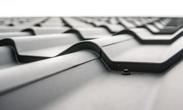 Detaljerad vy av ett tak med svarta, profilerade plåtar. En skruv syns i förgrunden, redo att fästa plåten. Perfekt för att måla galvad plåt.