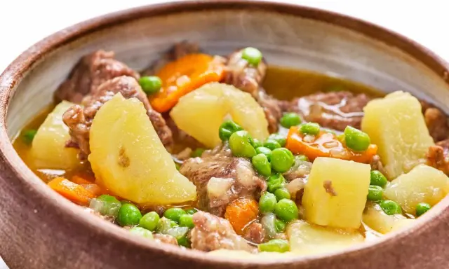 Un reconfortante ragout de ternera con patatas, zanahorias y guisantes en un cuenco rústico.