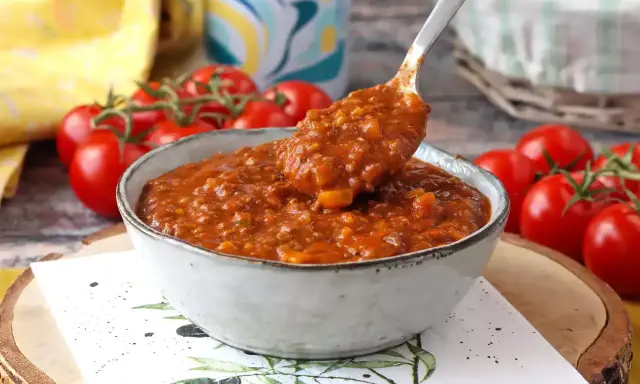 En skål med mustig bolognese, perfekt för ett gott bolognese recept. Färska tomater i bakgrunden.