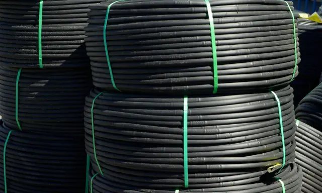 Rouleaux de tube plastique flexible noir, attachés par des sangles vertes, prêts pour l'irrigation.