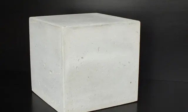 Ein Würfel aus hellem Beton C30/37 steht auf schwarzem Untergrund.