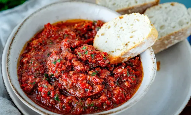 Schüssel mit würzigem Acili Ezme, einem scharfen türkischen Dip aus Tomaten und Paprika, serviert mit frischem Brot.