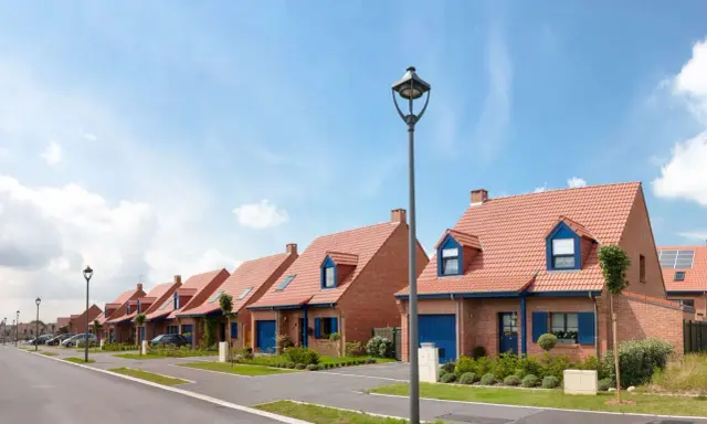 Vue d'une rue bordée de maisons de lotissement aux toits rouges et volets bleus, sous un ciel d'été.