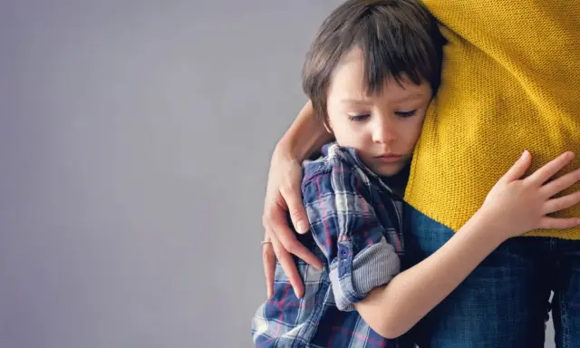 Niño de 6 años abraza a su madre con apego excesivo, buscando consuelo en su abrazo protector.