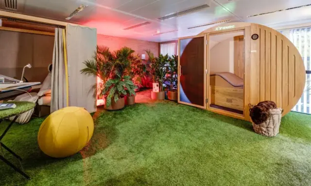 Une salle de pause originale avec un gazon synthétique, une cabine en bois, des plantes et un fauteuil de massage.