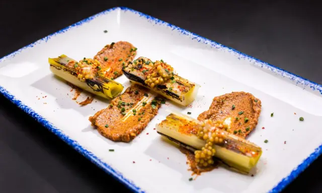 Puerros a baja temperatura, tiernos y dorados, servidos con una sabrosa salsa y granos de mostaza.