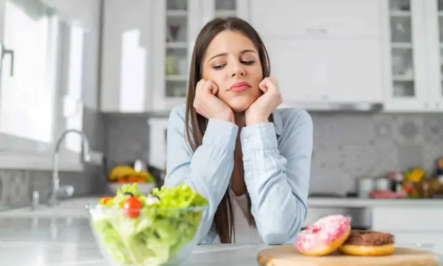 Femme triste face à une salade et des donuts, pensant aux aliments à éviter pour la dermite séborrhéique.