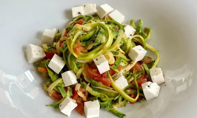 Spaghetti di zucchine freschi con pomodoro e cubetti di feta, conditi con pepe nero.