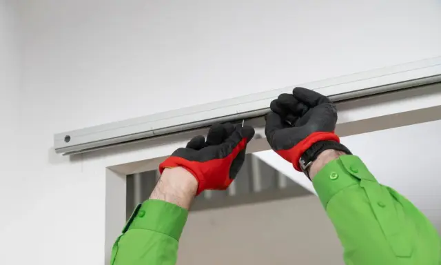 Man con guantes rojos y negros instala riel para puerta corredera.