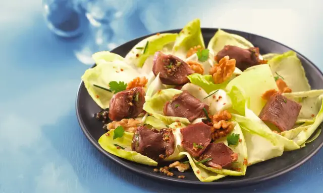 Salade de gésiers savoureuse avec endives croquantes, noix et persil frais, assaisonnée d'une vinaigrette aux graines.