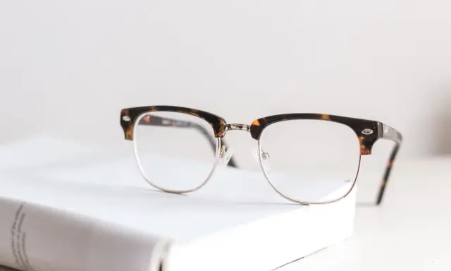 Okulary w stylu retro leżą na białej książce. Zastanawiasz się, od ilu dioptrii trzeba nosić okulary?