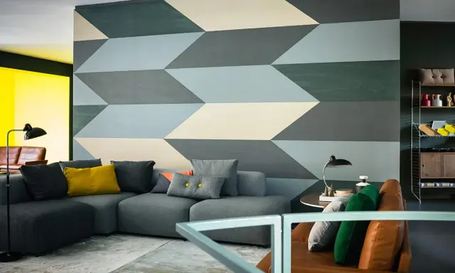 Un salon moderne avec un canapé gris et un mur orné d'un motif géométrique audacieux. Une idée motif peinture murale qui crée une illusion de profondeur.