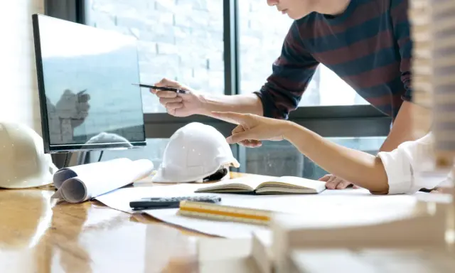 Deux architectes discutent d'un plan sur un écran, utilisant un système de gestion de contenu d'entreprise pour organiser leurs documents.