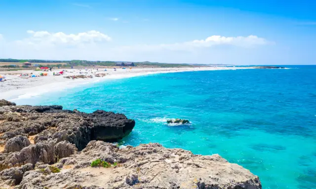 Scogli vulcanici e sabbia bianca su una spiaggia pop corn in Sardegna, con acque turchesi cristalline.