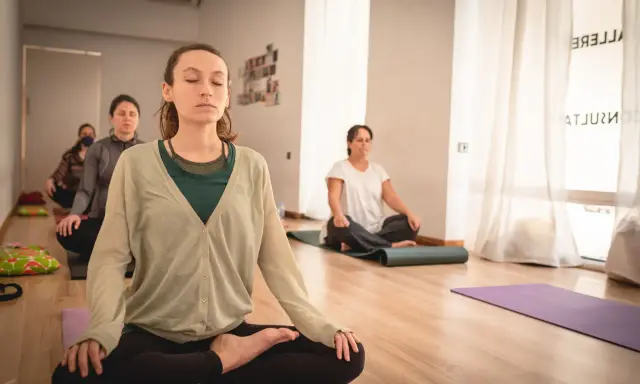 Mujeres meditando en clase de yoga. Una de ellas, en primer plano, parece estar en el **primer trimestre de embarazo**, buscando calma y conexión.