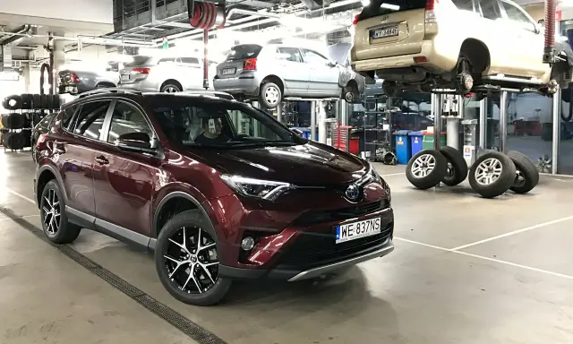 Czerwona Toyota RAV4 w serwisie. W tle inne auta na podnośnikach. Zastanawiasz się nad toyota trzeci przegląd gwarancyjny cena?