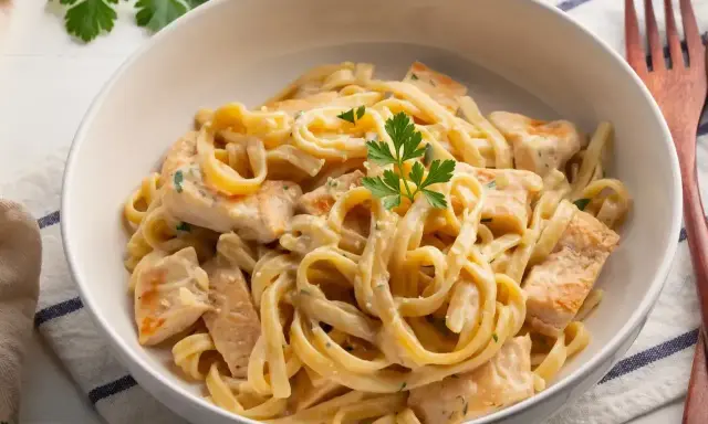 Pyszne makaron tagliatelle z kurczakiem w kremowym sosie, udekorowane natką pietruszki. Idealne danie na obiad.
