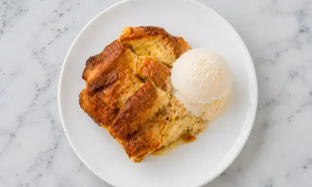 Un délicieux pain perdu au four, doré et moelleux, servi avec une boule de glace à la vanille sur une assiette blanche.