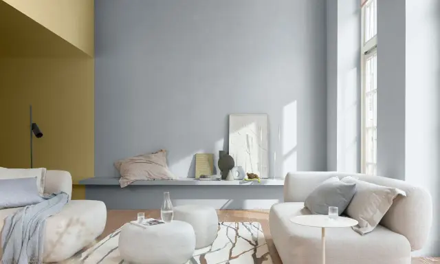 Sala de estar con paredes en tonos grises y mostaza, muebles claros y alfombra con diseño orgánico. Ideales colores suaves para pintar una casa.
