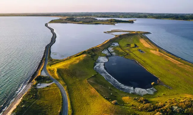 Grönskande landskap med en slingrande väg längs kusten i Danmark. En vy som från ett utkikstorn Danmark, med vatten och fält.