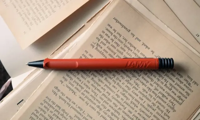 Un stylo rouge Lamy repose sur des pages jaunies. Force est de constater que la lecture et l'écriture font partie de notre histoire.