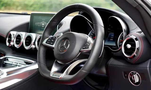 Interior de un coche deportivo Mercedes-AMG. Volante de cuero negro con controles, logo de Mercedes y detalles AMG.