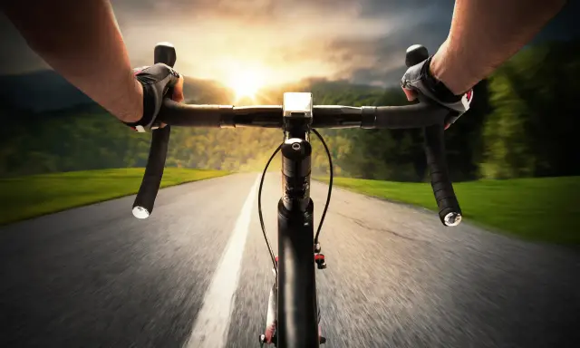 Rowerzysta w rękawiczkach pędzi po asfalcie. Słońce zachodzi, a krajobraz rozmywa się w tle. Ile czasu zajmie mu przejechanie 100 km rowerem?