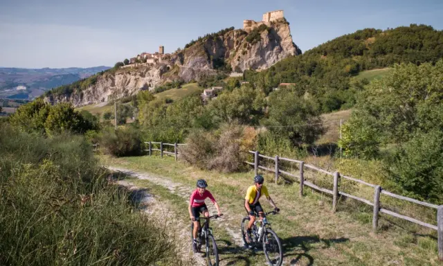 Ciclisti su una ciclabile panoramica con un borgo fortificato in lontananza, un'avventura tra le colline vicino a Rimini.