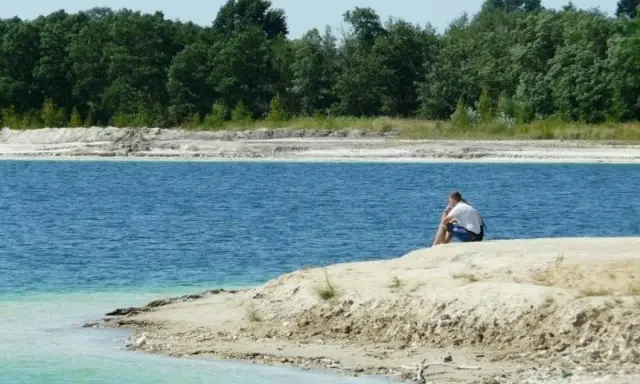 Samotny mężczyzna siedzi nad turkusową wodą, która przypomina polskie Malediwy łódzkie.