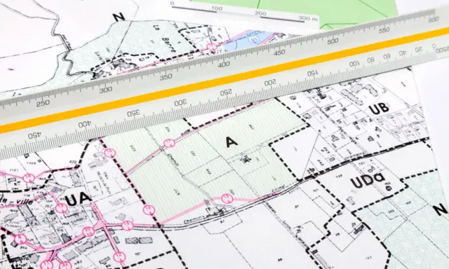 Plan zagospodarowania przestrzennego z naniesionymi strefami i podziałami. Linijka geodezyjna pomaga w precyzyjnych pomiarach.