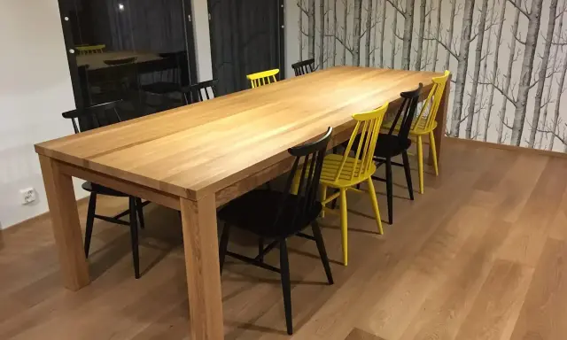 Stilleben matbord i trä med svarta och gula stolar. Bakom syns en fondvägg med trädmotiv.