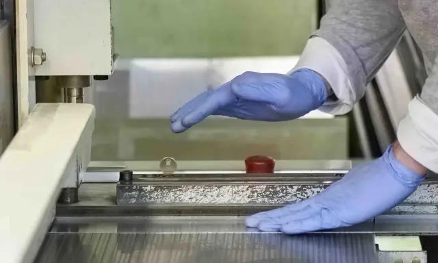 Manos enguantadas operan una máquina que parece ser una cizalla, lista para cortar material.