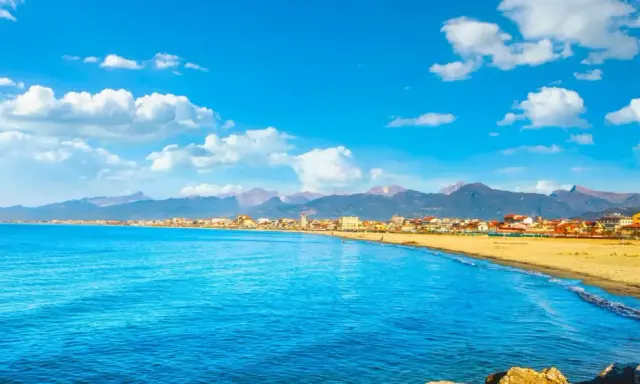 Spiaggia dorata e mare azzurro a Viareggio, con montagne sullo sfondo. Perfetto per scoprire cosa vedere a Viareggio in un giorno.