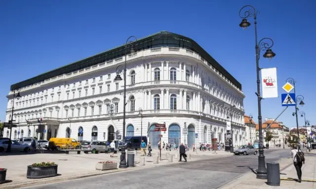 Elegancki, biały budynek w centrum Warszawy, być może najdroższy hotel w Warszawie. Słoneczny dzień, ruch uliczny.