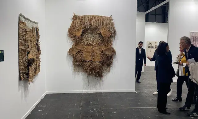 Exhibición de arte contemporáneo con tapices texturizados y personas observando.