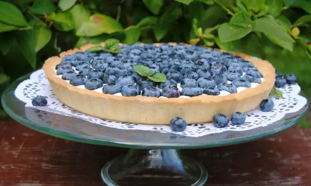 Pyszna tarta z borówkami, udekorowana listkami mięty, prezentuje się apetycznie na szklanej paterze.
