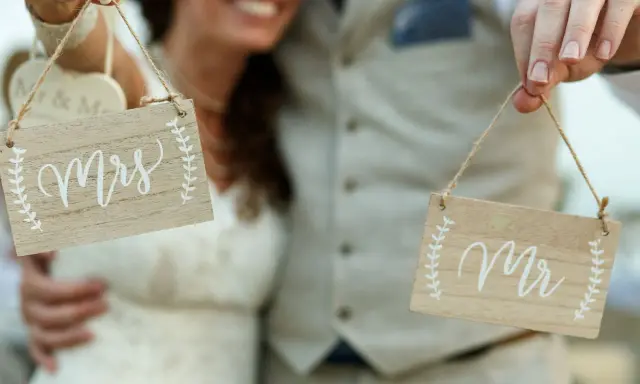 Para Młoda trzyma tabliczki "Mrs" i "Mr", symbolizujące zmianę nazwiska po ślubie.