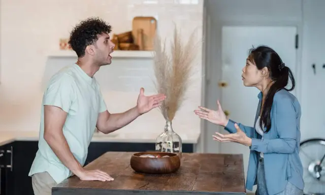 Pareja discutiendo en la cocina, un momento de reflexiones de pareja en crisis. Sus gestos y expresiones muestran tensión.