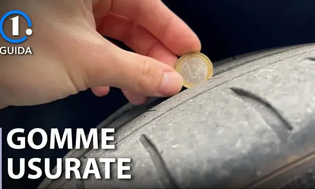 Una mano inserisce una moneta da 1 euro in un solco di uno pneumatico per mostrare come vedere se le gomme sono consumate.