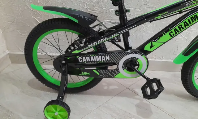Czarny rower dziecięcy z zielonymi akcentami i napisem "CARAIMAN". To świetny rower dla początkujących.