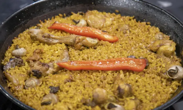 Paella de arroz con carne, pimientos rojos y caracoles. Un plato tradicional español lleno de sabor.