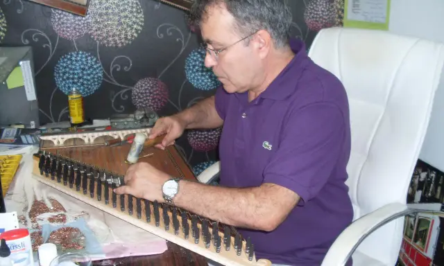 Un artisan ajuste les cordes d'un kanun, instrument de musique traditionnel, avec un marteau.