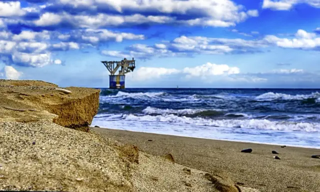 Sandige Klippen am playa del cable, mit einer Plattform im Meer unter dramatischem Himmel.
